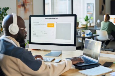 Kulaklıklı genç ciddi bir adam yeni yazılım üzerinde çalışırken laptop ve masaüstü bilgisayarlarının tuşlarına basıyor