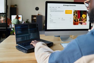 İki masaüstü bilgisayarına ve veri çözerken dizüstü bilgisayarda yazan genç erkek programcının eline odaklan