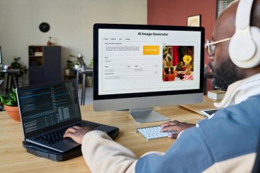 Genç Afrikalı Amerikalı bir adam yeni yazılımı işyerine göre kullanırken veya test ederken iki masaüstü bilgisayarının tuş takımlarını kullanıyor