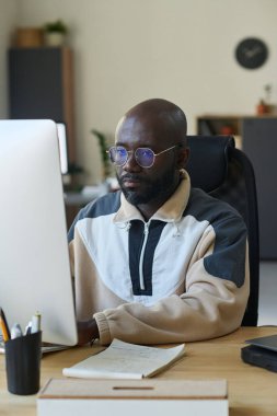 Afrikalı Amerikalı erkek yazılım geliştirici bilgisayar monitörü önünde otururken ve ekrana bakarken yeni ürün üzerinde çalışıyor