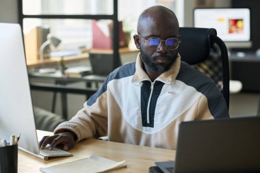 Genç Afrikalı Amerikalı adam ofiste ağ kurarken dizüstü bilgisayara bakıyor ve tuş takımına dokunuyor