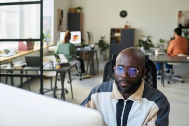 Yeni ürünü test ederken veya veri çözerken masaüstü bilgisayarına bakan kel Afrikalı Amerikalı yazılım geliştiricisi