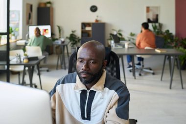 Genç, ciddi bir Afro-Amerikan programcı. Masaüstü bilgisayarının önünde işyerinde oturuyor ve ekrana bakıyor.