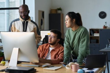 Üç kültürler arası tasarımcı veya programcı birlikte çalışma alanındaki bilgisayar ekranında yeni yazılım ürünlerine bakıyor