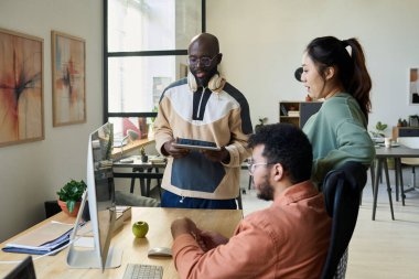 Üç genç kültürler arası çalışan masaüstü bilgisayarının önünde toplanarak yeni çalışma projesinin noktalarını tartıştılar.