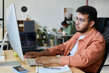 Ciddi genç erkek yazılım geliştirici veya tasarımcı bilgisayar tuş takımının tuşlarına basıyor ve çevrimiçi bilgilere bakıyor