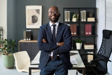Kurul odasında kameraya gülümseyen takım elbiseli Afro-Amerikan işadamının portresi.