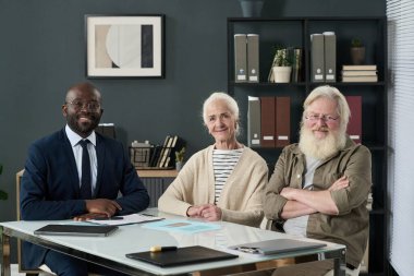 Ofisteki toplantıda finans danışmanıyla birlikte kameraya bakan yaşlı çiftin portresi.