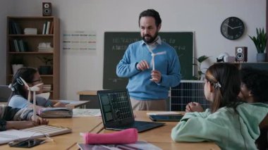 Kafkas erkek öğretmenin çeşitli küçük çocuklar için çevre eğitimi dersi verirken orta ölçekli rüzgar türbini modeli göstererek, operasyon fikrini açıklarken orta kavisli pozu.