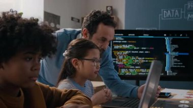 Orta boy beyaz erkek programlama öğretmeni masada oturan ve dizüstü bilgisayarla uğraşan genç Asyalı kıza doğru yürürken, algoritmayla boğuşurken, şifreli hataya işaret ederken, tavsiyeyle