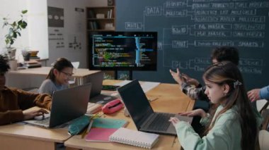 Orta yaşlı beyaz erkek programlama öğretmeninin sınıfta dolaşırken, çeşitli öğrencilerin dizüstü bilgisayarlarda görevlerini yerine getirirken, yararlı yorumlar yaparken ve geri bildirim yaparken tam bir fotoğrafı.