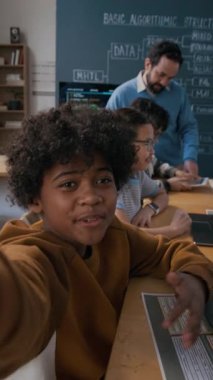 Sosyal medya paylaşımı için dizüstü bilgisayarlar üzerinde çalışan kıvırcık saçlı, neşeli 10 yaşındaki Afrikalı Amerikalı çocuğun orta dikey UGC görüntüsü.