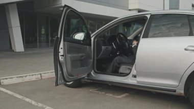 Şoför koltuğunda oturan ve parçalanmış tekerlekli sandalyeyi arabadan çıkaran iş adamının görüntüsü.