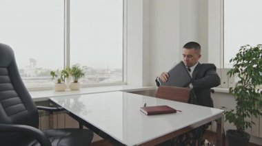 Tekerlekli sandalyedeki işadamının evraklarını ve planlayıcısını çantaya koyup ofisten çıkarken orta boy fotoğrafı.