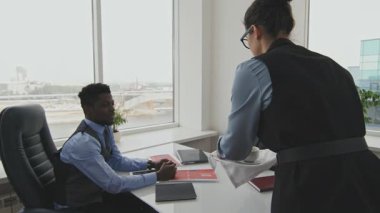 Afrika kökenli Amerikalı iş adamına kahve servisi yapan kadın kişisel asistanın ve tekerlekli sandalyedeki yöneticinin el kamerasıyla çekilmiş resmi.