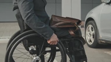 Tekerlekli sandalyedeki tanınmayan işadamının orta bölüm takibi. Arabasına doğru gidiyor, sonra kapıları açıyor ve çantasını sürücü koltuğuna koyuyor.