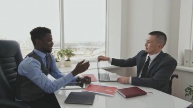 Afro-Amerikalı neşeli işadamının yan görüntüsü. Sandalyede oturan yöneticiyle gülümseyen ve tokalaşan.