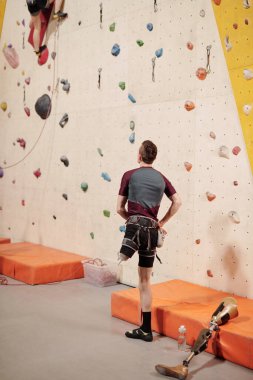 Duvara tırmanma eğitiminin önünde duran engelli genç adam.