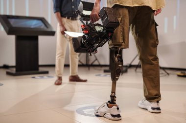 Stüdyoda Afrikalı adamın önünde duran robot bacaklı bir kameraman.