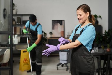 Lastik eldiven giyip ofiste çalışmaya hazırlanan bir temizlikçi.