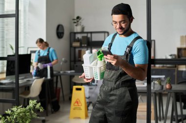 Temizlikçi üniformalı, ofiste temizlik yaparken akıllı telefondan mesaj yolluyor.