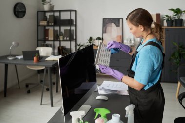 Ofis temizliği sırasında bilgisayar ve masadaki tozları silen işçiler