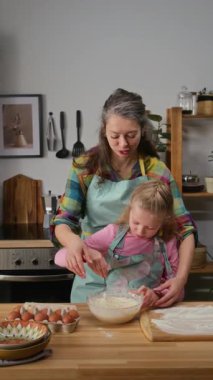 Önlüklü neşeli, olgun, beyaz bir annenin, küçük kızına mutfakta kurabiye ya da kek çırpmayı öğretirken, hafta sonları birlikte kaliteli vakit geçirmenin keyfini çıkardığı orta boy dikey pozlar.