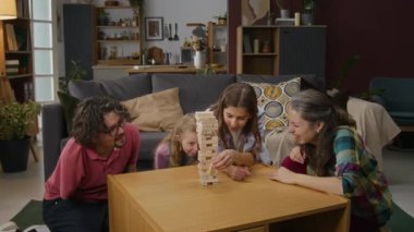 Orta yaşlı beyaz bir çocuk başarılı bir şekilde tahta bloğu kulenin tepesine çıkarırken anne, engelli bir baba ve küçük kız kardeşi de izliyor, alkışlıyor ve alkışlıyor.