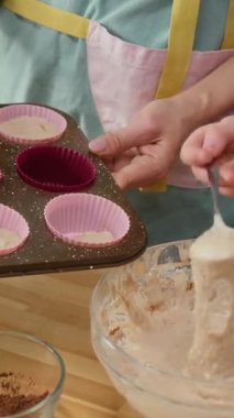 Önlüklü, elinde kek tepsisi olan tanınmayan bir annenin elleri ve çay saati için tatlı pişirirken kalıpları hamurla dolduran isimsiz bir çocuğun orta boy dikey görüntüsü.