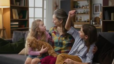 Orta halli, bekar anne, ergen oğul ve genç kızın, evdeki kanepede evcil maltipoo köpeğiyle birlikte rahatlarken, sarılırken, sarılırken ve öpüşürken.