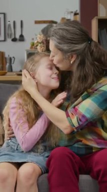 Yetişkin, bekâr bir anne ve genç kızın kanepede rahatlarken, sarılırken, öpüşürken, sohbet ederken ve gizli şeyleri paylaşırken orta boy dikey görüntüsü.