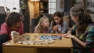 Orta boy, çeşitli, beyaz bir ailenin oyun oynayıp birlikte hareket ettiği bir fotoğraf. Genç çocuk zar sallıyor, atıyor, kaybediyor. Kız kardeşi ise neşeyle kazanıyor ve tezahürat yapıyor.