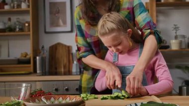 7 yaşında neşeli bir sarışının salata için domates ve salatalık kesmeyi öğrendiği orta ölçekli bir pozu.