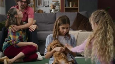 Orta büyüklükte mutlu bir beyaz aile evcil köpekle el çırpma oyunu oynarken, engelli bir koca ve karısı sarılıp sohbet ediyor.