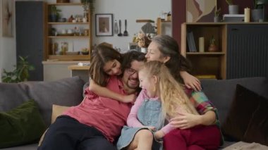 Orta halli mutlu beyaz bir baba, kolları kayıp, sevgi dolu bir anne, genç bir oğul ve kız, aile evinde kanepede oturuyor, sarılıyor, sarılıyor, gıdıklıyor ve gülüyor.