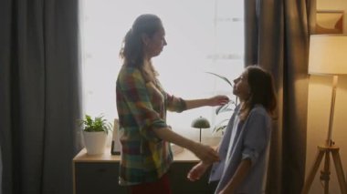 Orta yaşlı, beyaz bir anne ve gencin birbirine sarılıp öpüştüğü, aile evinin parlak güneşli penceresinin önünde birbirini seven orta yaşlı beyaz bir çocuk.