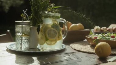 Açık hava partisi ya da güneşli bir yaz günü güneşli bir günde barbekü için hazırlanmış bahçe masasında, bir demet yabani çiçeğin yanında taze yapılmış soğuk limonata içeceğinin cam kavanozuna yakın çekim.