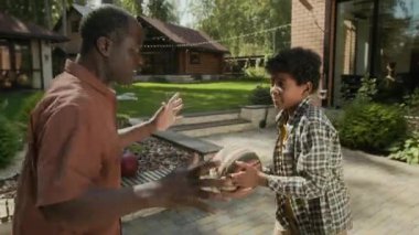 Orta boy Afro-Amerikan bir çocuğun babasıyla basketbol antrenmanı yaparken, top oynarken, top oynarken, basket atarken, gol atarken ve babaya beşlik çakarken.