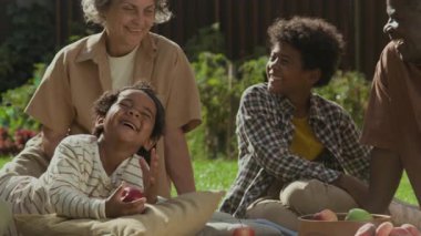 Orta büyüklükte Afrika kökenli beş çocuklu neşeli Amerikalı aile bahçedeki çimenlerde dinleniyor, piknik yapıyor, şakalaşıyor ve gülüyor.