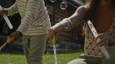 Orta boylu, neşeli 14 yaşındaki Afrikalı Amerikalı kız ve 6 yaşındaki erkek kardeş uzun çubuklarla gökkuşağı sabun köpüğü yaparken açık havada güneş ışığında birlikte oynuyorlardı.