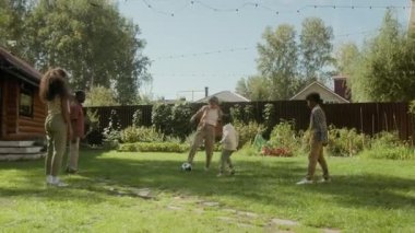 Geniş açılı mutlu, çoklu etnik kökenli bir aile annesi, Afrikalı Amerikalı bir baba ve üç melez çocuk güneşli bir günde yeşil çimlerde futbol oynuyorlar.