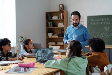 Modern sınıf ortamında, teknoloji ve grup öğrenme dinamiklerine odaklanmış çeşitli dijital tasarım gruplarını eğiten öğretmen.