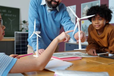 Öğretmen sınıfta hevesli öğrencilere rüzgar enerjisinin faydalarını anlatıyor. Sürdürülebilirlik ve yenilenebilir enerji kavramları derslerine aktif olarak katılan odaklanmış öğrenciler