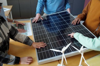 Büyük güneş panelinin etrafında toplanan bir grup insan, bunun özelliklerini ve faydalarını birebir olarak ele alarak, yenilenebilir enerji eğitimine olan katkısının altını çizdi.