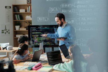 Öğretmenler sınıftaki özenli öğrencilere dizüstü bilgisayar ve eğitim materyalleriyle dolu kodlama kavramlarını anlatıyor, işbirlikçi öğrenme ortamı sergiliyor