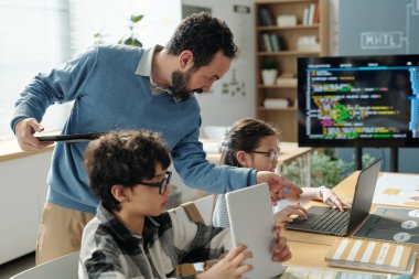 Açık dizüstü bilgisayarlar ve etkileşimli atmosfere katkı sağlayan eğitim araçlarıyla parlak ışıklandırılmış sınıflarda öğrencilere programlama öğrenmesinde yardımcı olan öğretmen