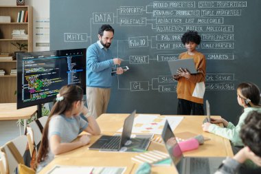 Öğrenciler sınıf ortamında dizüstü bilgisayarlarla uğraşırken, öğretmenler dijital ekran kullanarak moleküllerin özelliklerini açıklıyorlar