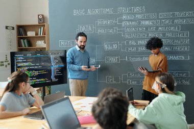 Sınıfta tebeşir ve akıllı tahta kullanarak ilgili öğrencilere algoritmik yapıları açıklayan eğitmen. Çeşitli öğrencilerden oluşan bir grup kodlama kavramıyla ilgileniyor