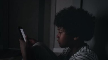 Afrika kökenli çaresiz bir çocuğun karanlık koridorda çömelmiş, akıllı telefondaki zorbalardan gelen acımasız mesajları okurken, ağlayarak elleriyle yüzünü gömerken yakın plan çekimleri.