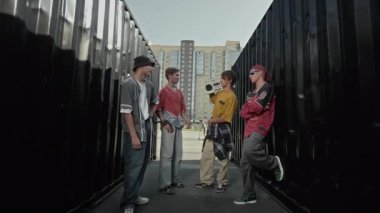 Hip hop kıyafetleri içinde, şehrin varoşlarında eski moda müzik kutusuyla koridorda dikilirken sohbet eden dört şık beyaz çocuğun portresini büyüt ve kendine güvenen bir havayla kameraya bak.